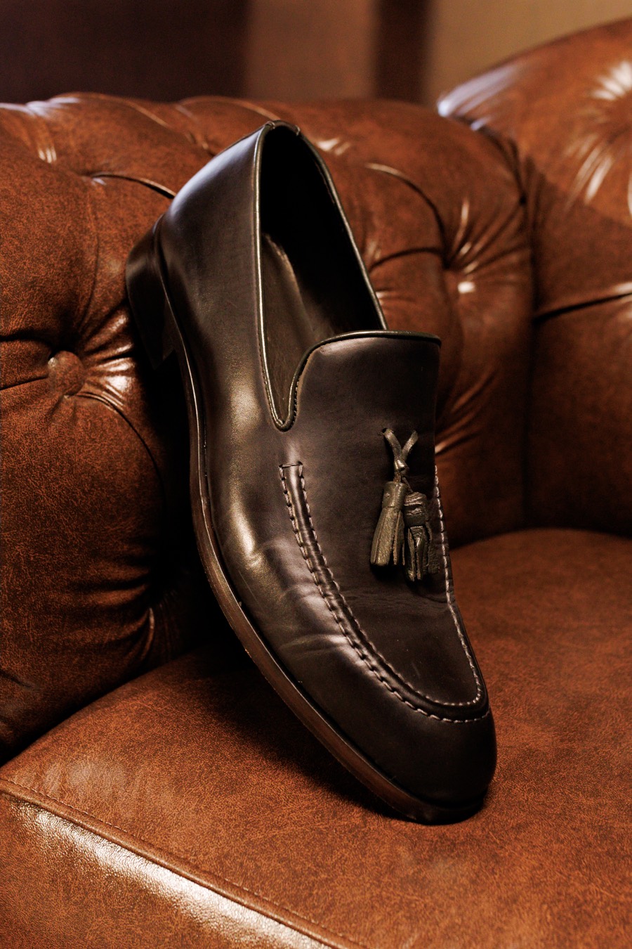 Loafer masculino de couro preto com franjas sobre poltrona de couro